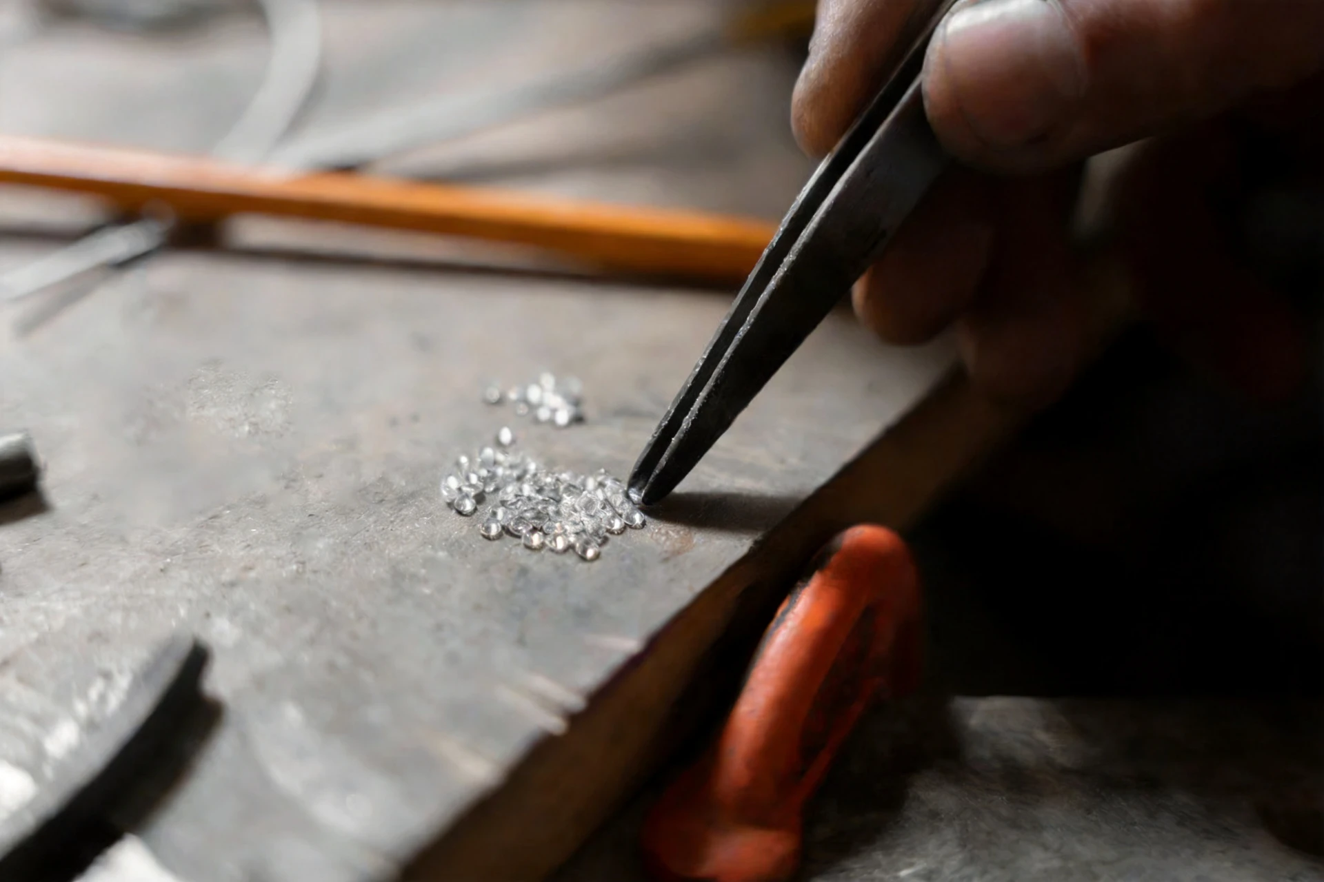 A goldsmith sorting loose brilliant-cut diamonds with tweezers at the workbench